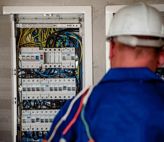 Electrician with a hard hat in front of an open electrical distribution board
